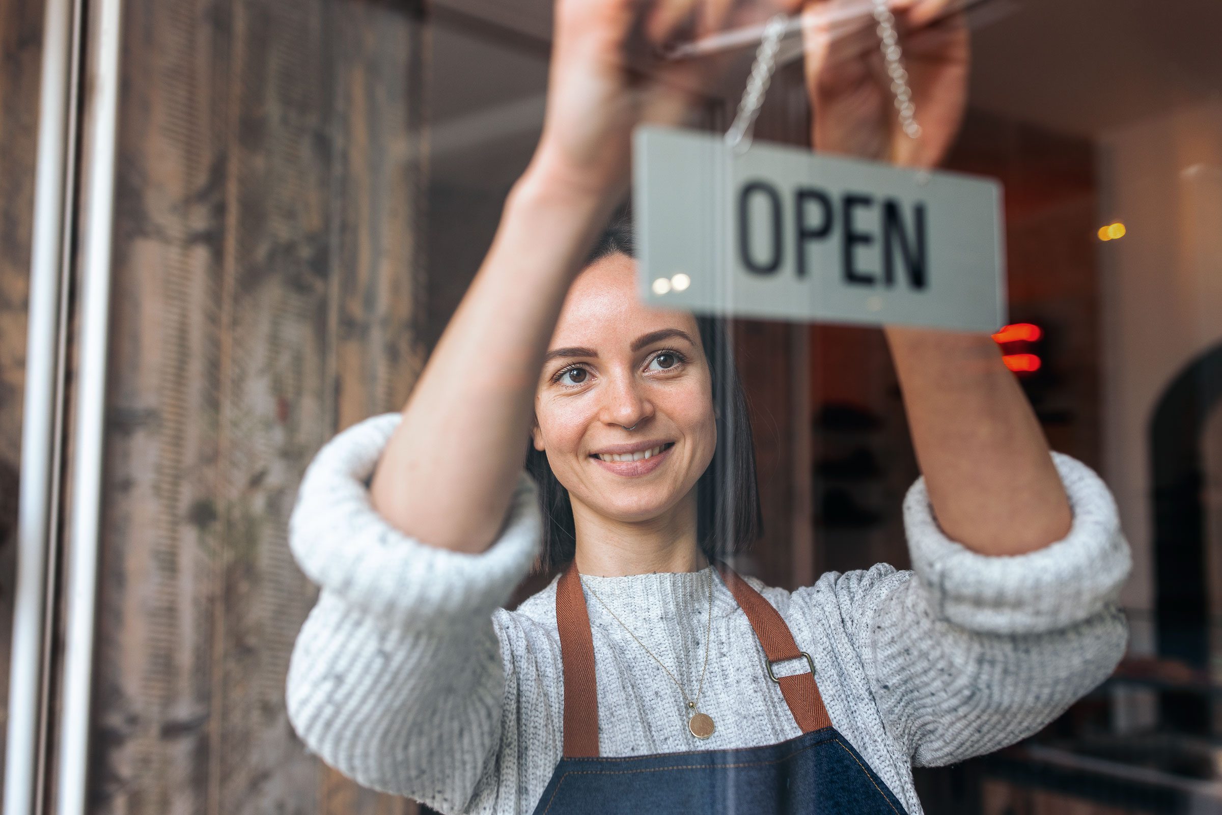 Eine Frau hält ein "Geöffnet"-Schild vor einem Geschäft.