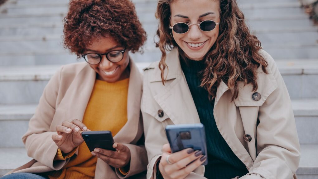 Zwei Frauen sitzen auf Treppenstufen und lesen die News.