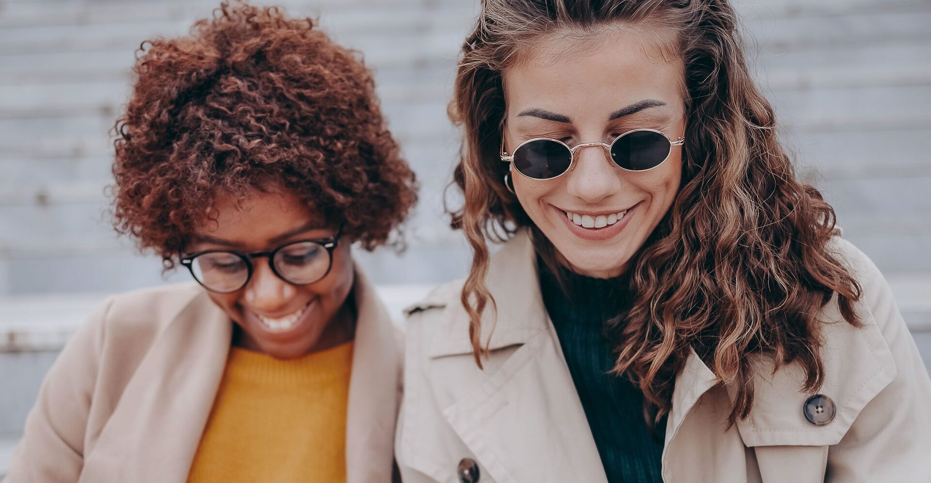 Zwei Frauen sitzen auf Treppenstufen und lesen die News.