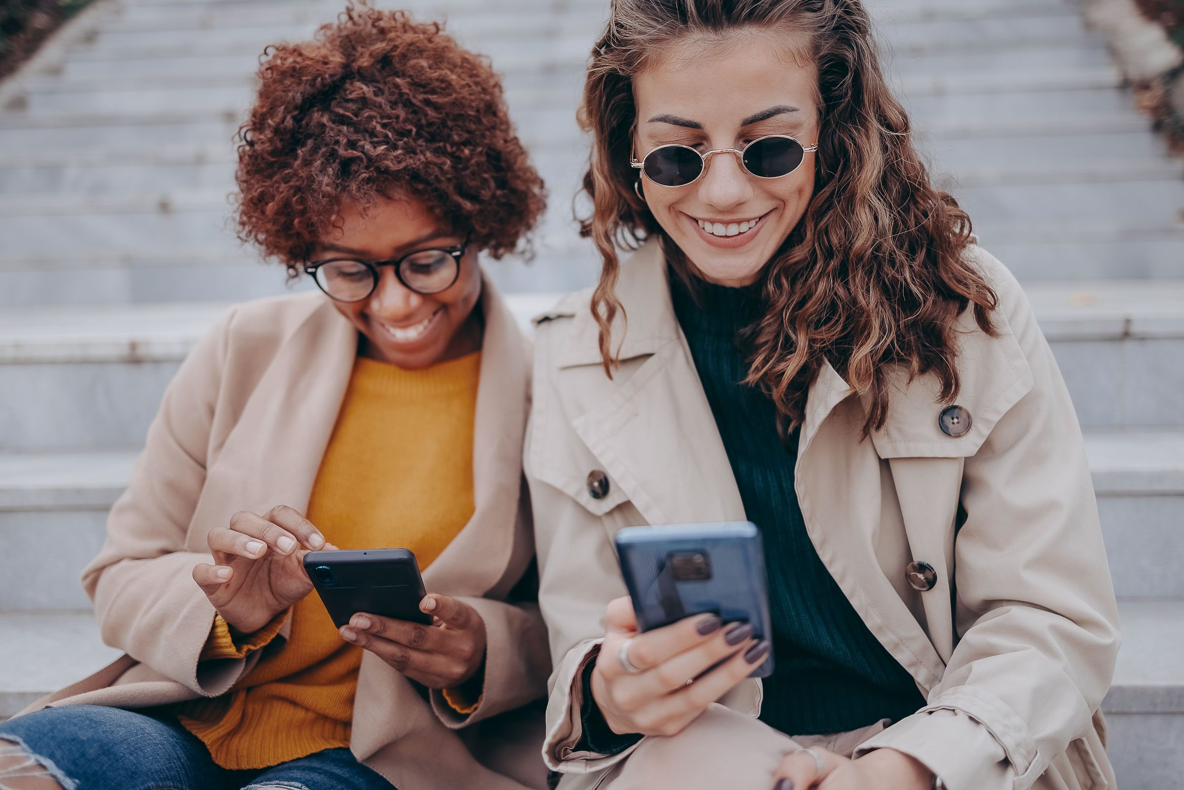 Zwei Frauen sitzen auf Treppenstufen und lesen die News.