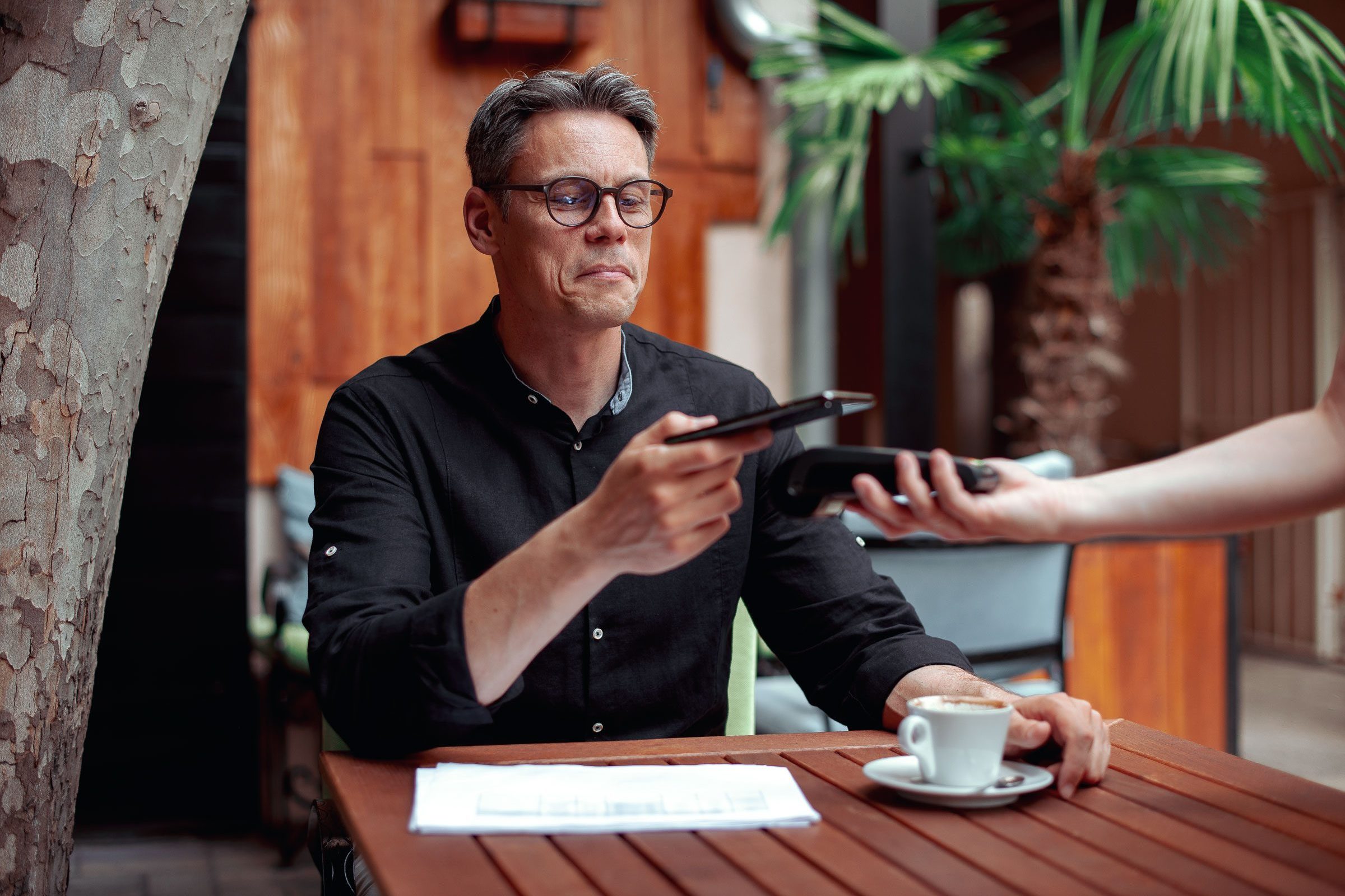 Ein Mann sitzt an einem Tisch mit einer Tasse Kaffee und bezahlt mit Mobilepayment.