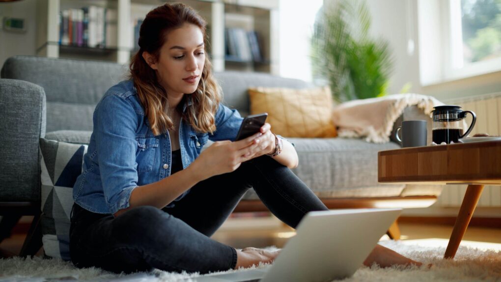 Frau sitzt im Wohnzimmer auf dem Boden und benutzt die ZLB Mobile Banking App.